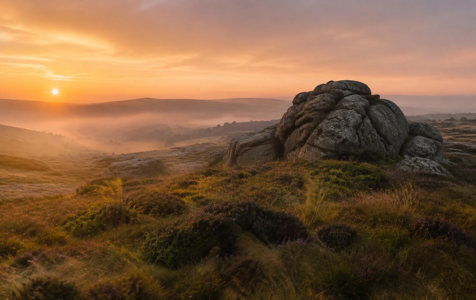 Dartmoor tor at golden hour with mist in the valleys